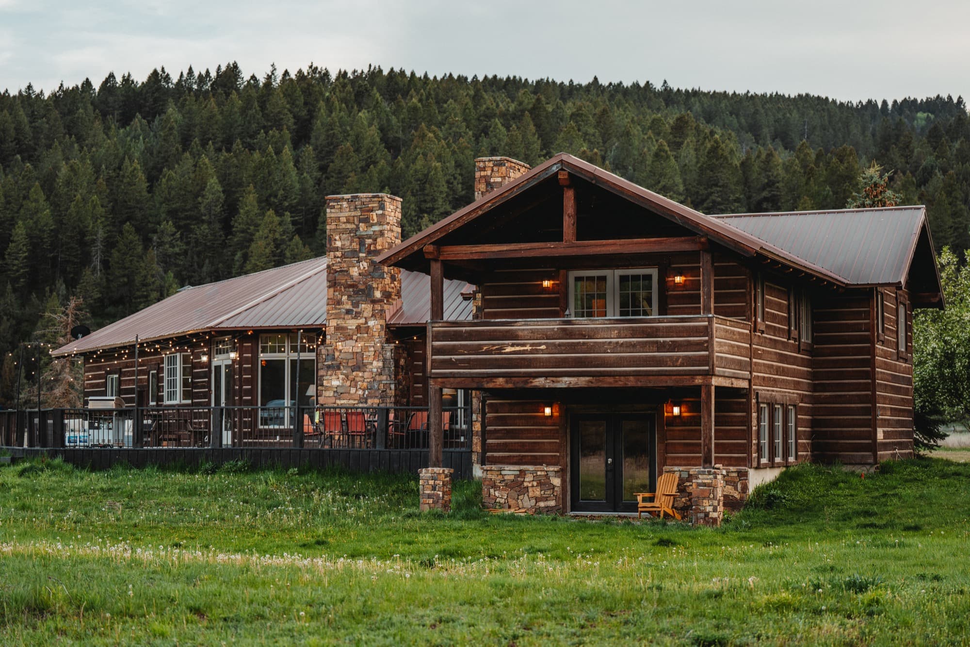 Log cabin with stone chimneys against a forested hillside in Swan Valley, Idaho